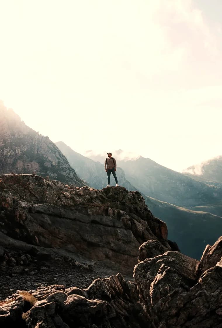 A hiker standing on a rocky ridgeline before sunlit peaks
