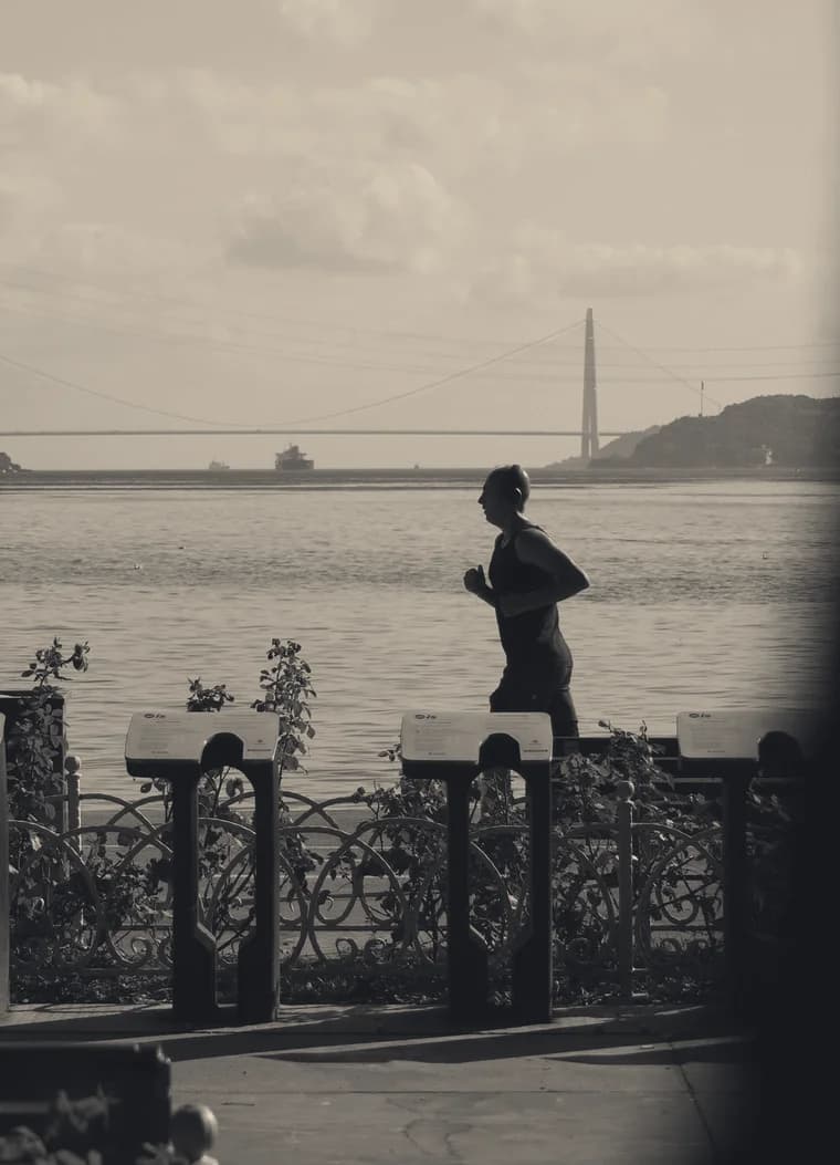 A runner in stride along a waterfront promenade, suspension bridge behind